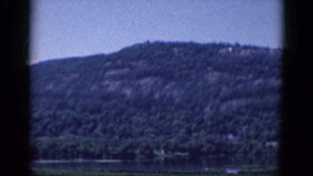 Wooded hillside above a narrow lake shoreline, seen through film-frame borders.