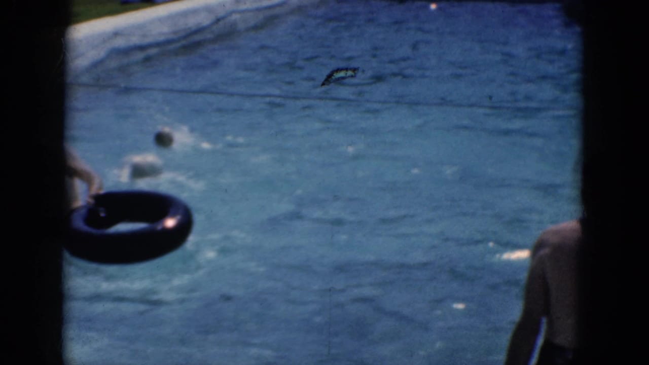 Swimmer holds a dark inner tube near the pool wall while a ball floats nearby.