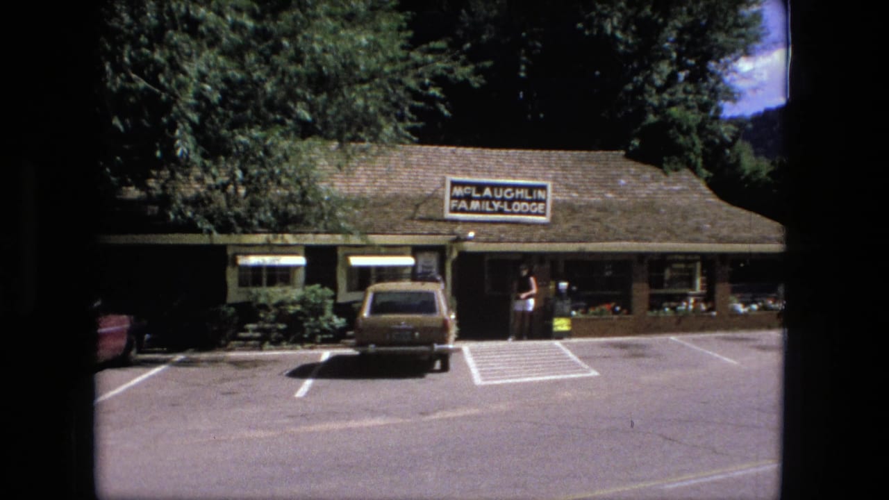 Motel exterior with McLaughlin Family Lodge sign, station wagon, and woman near the entrance.