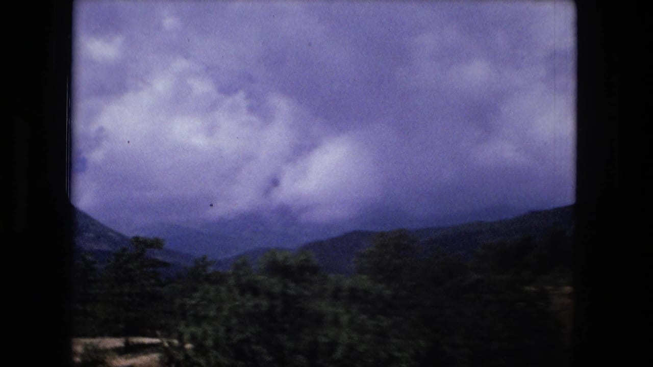 Cloudy mountain ridges with trees in the foreground and dark film borders.