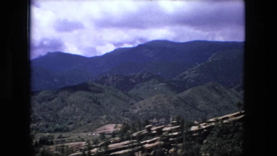 1970s 8mm frame looking across layered green hills toward darker mountains, with faint valley details below.