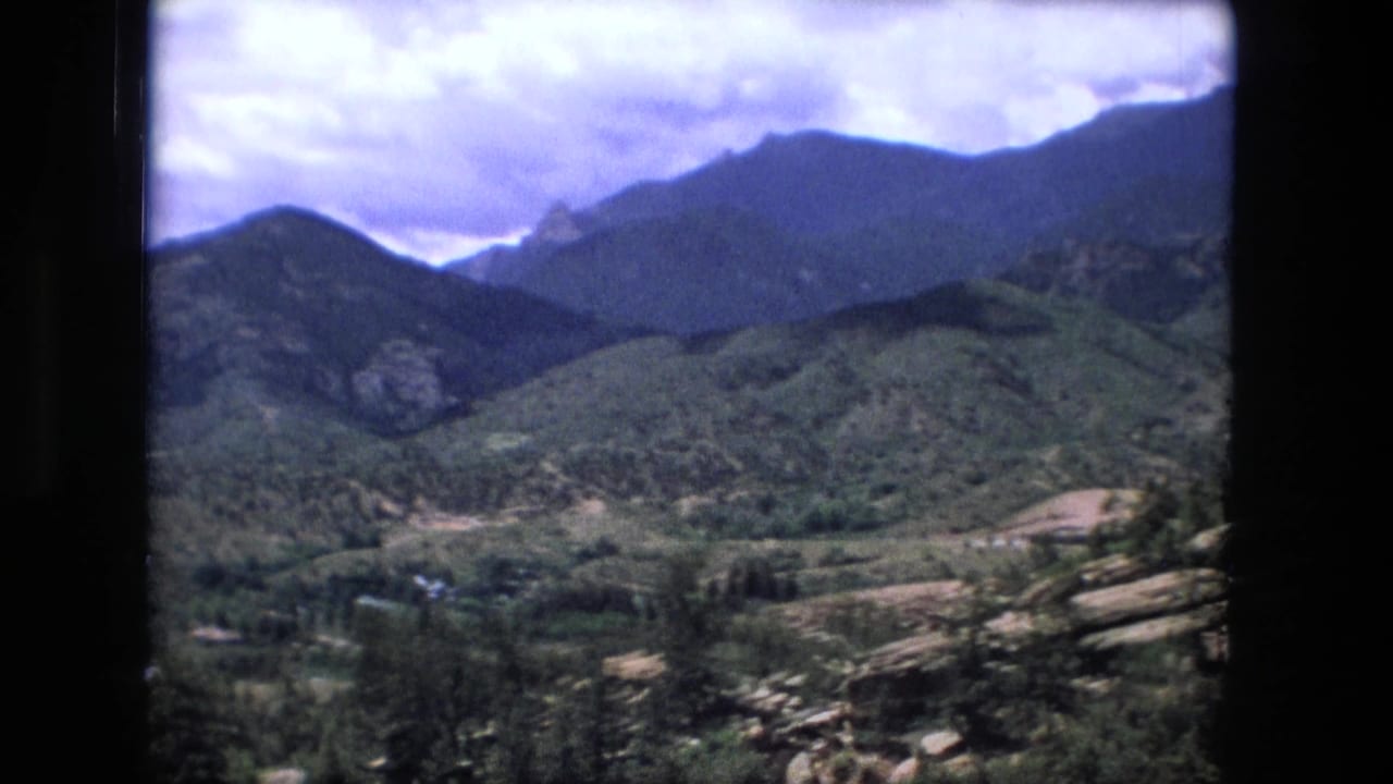 Forested mountain valley beneath a cloudy sky, seen through dark 8mm frame borders.