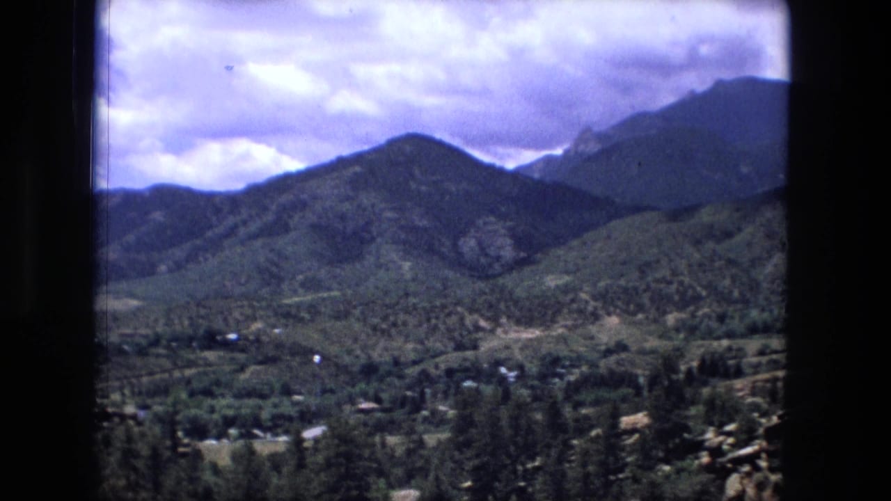 Mountain ridge and green valley with scattered homes under bright clouds.
