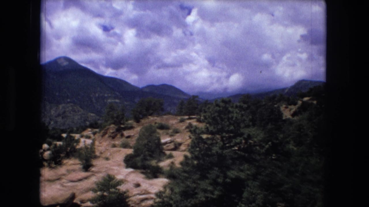 Wooded hillside with rocky slopes, distant mountains, and a cloudy sky.