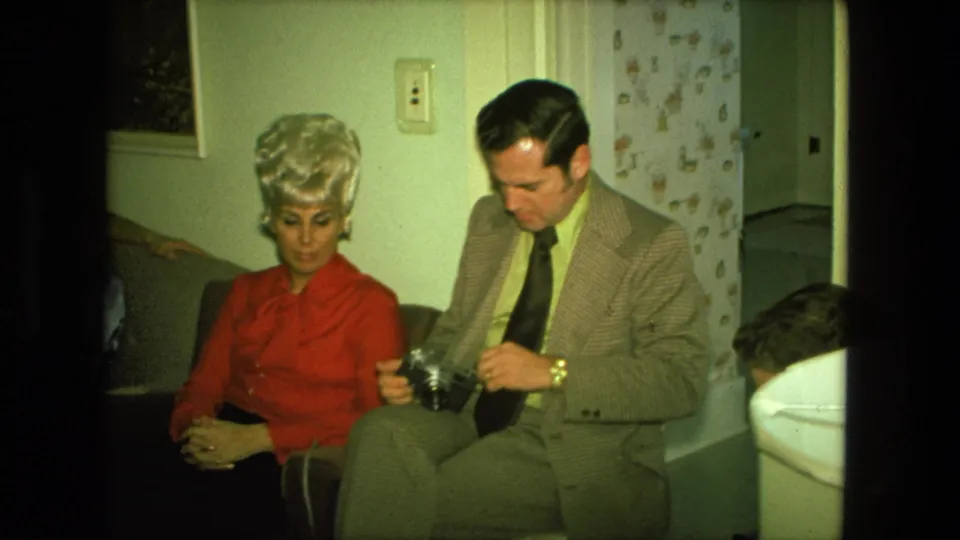 The final frame shows the Fort Wayne home interior with the woman in red and the suited man still focused on the camera.