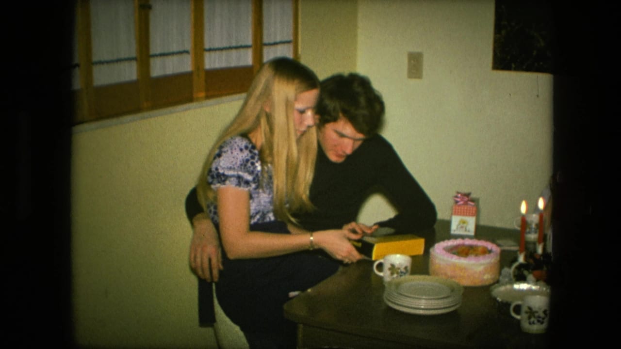 Young woman sitting on a young man's lap beside a birthday cake and candles.