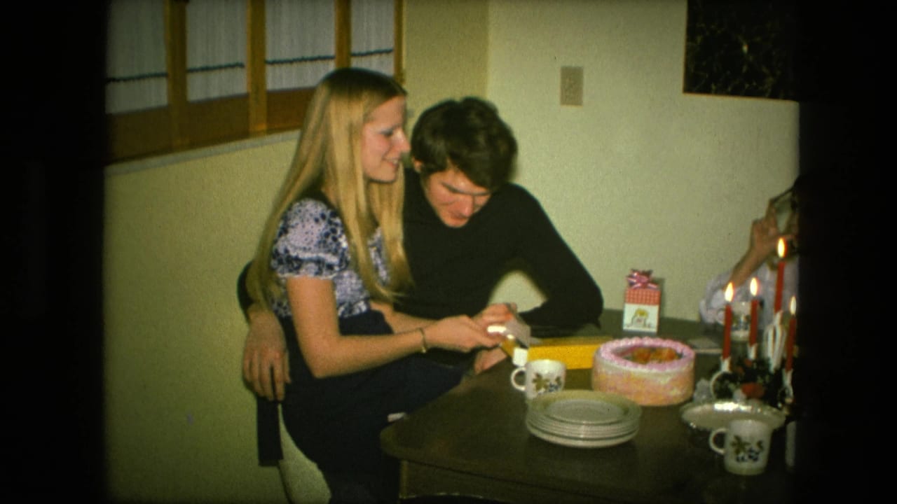 The young couple smiles while opening a yellow gift box beside a birthday cake and lit candles in 1976 Fort Wayne footage.