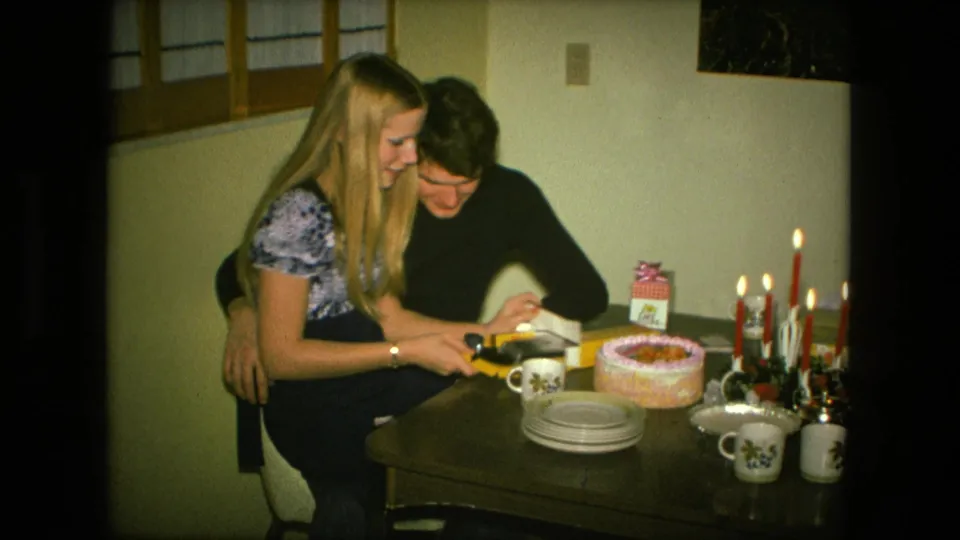 The couple examines the opened yellow box at a birthday table in a private Fort Wayne interior, with cake and candles visible.