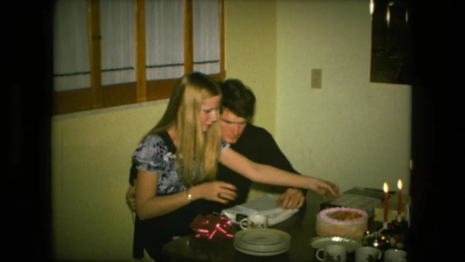 A young couple in a Fort Wayne home leans over gift materials and table settings during a small birthday celebration.