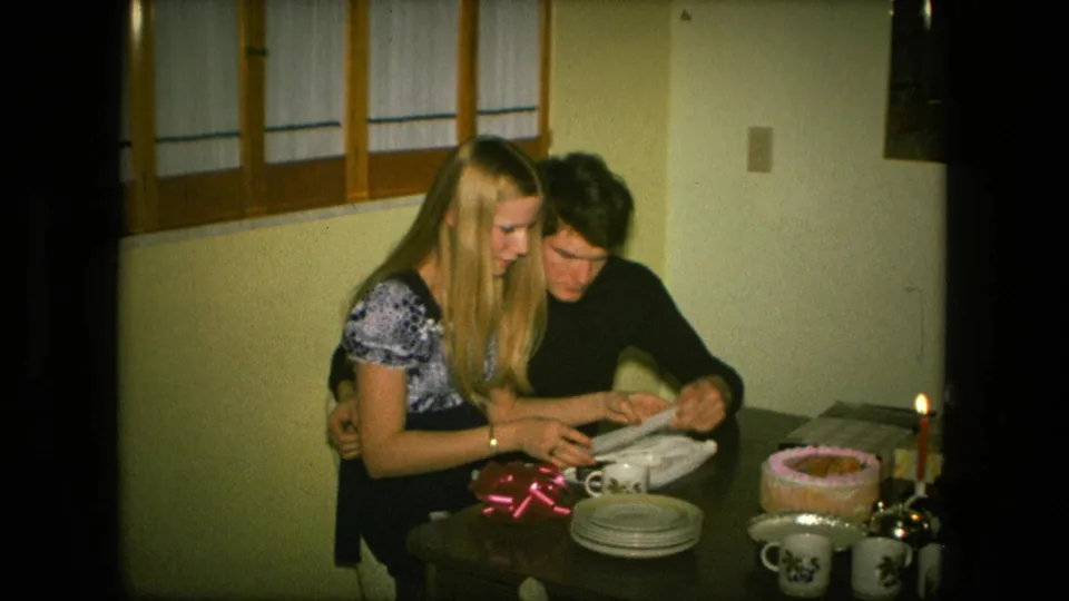 The 1976 home-movie frame shows the couple seated together at a Fort Wayne birthday table after opening the gift.