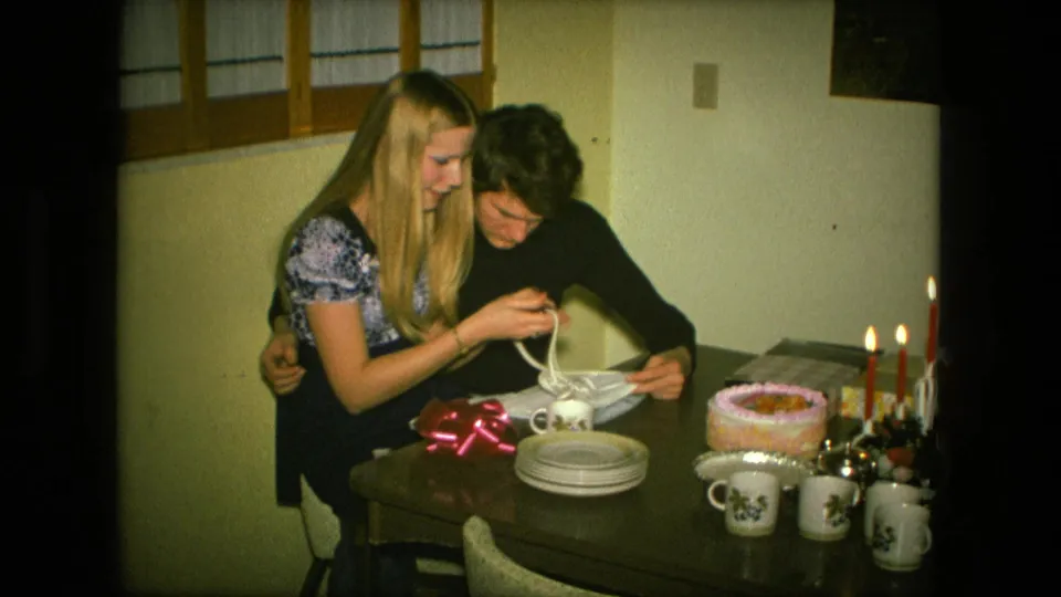 The young couple smiles together in the Fort Wayne home-movie birthday scene while handling the opened gift at the table.