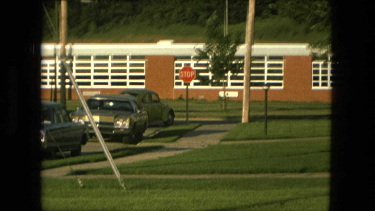 Parked cars near a brick school building with white window bands and a stop sign.