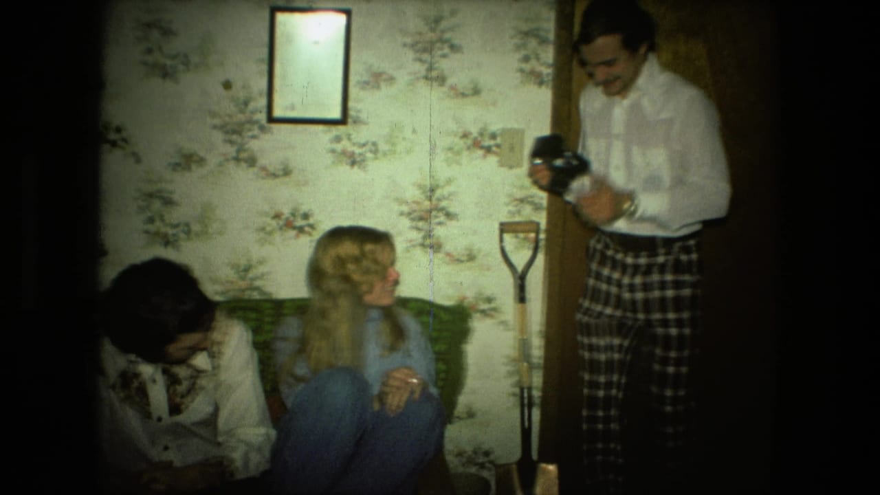 Three adults in a living room as a man holds a camera near a couch.