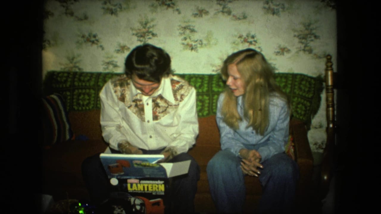 A 1976 Fort Wayne living room scene shows a young man inspecting a Coleman lantern box while a blonde woman leans in with interest.
