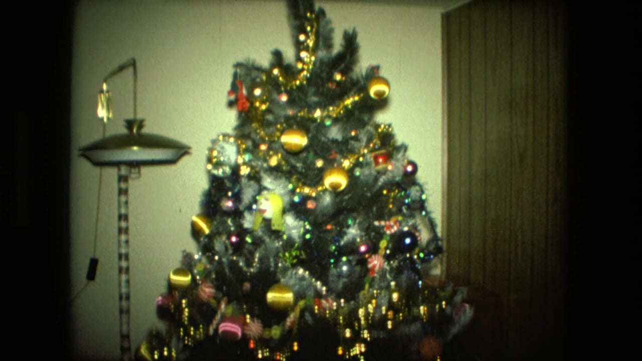Decorated Christmas tree beside a floor lamp and wood-paneled wall.
