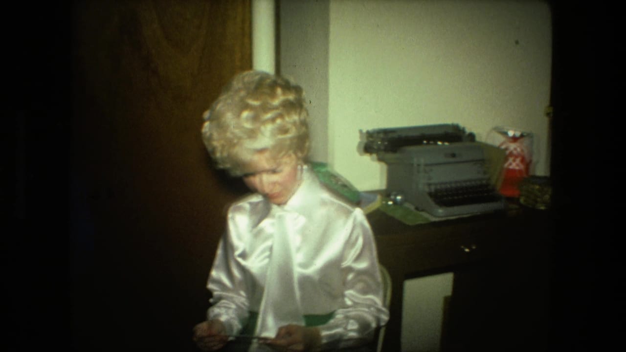 Woman in a white satin blouse sits indoors opening an envelope near a manual typewriter.