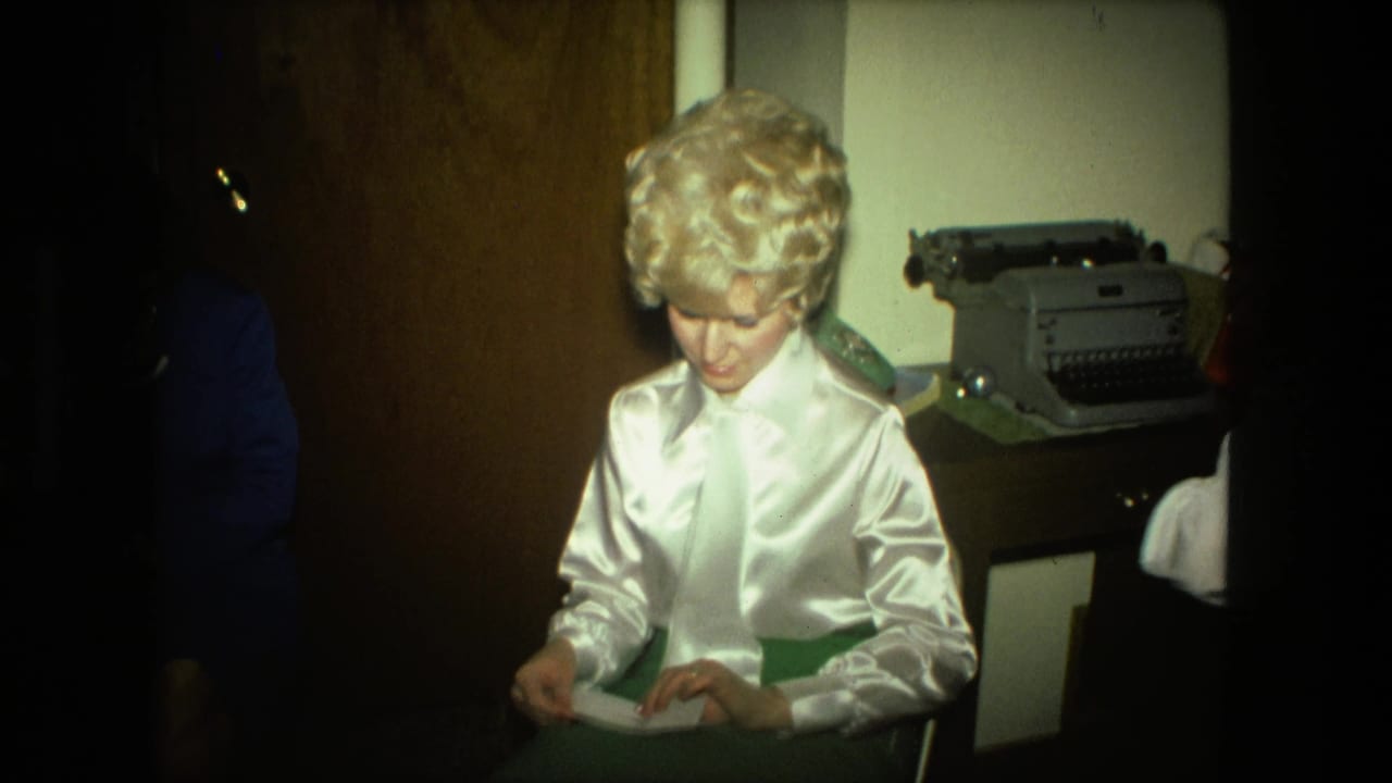 The woman continues handling the envelope in the Fort Wayne interior, framed beside wood paneling and a gray manual typewriter.