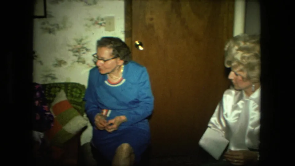 A later frame shows women seated in a private living room with floral wallpaper, wood paneling, and the envelope still visible at right.