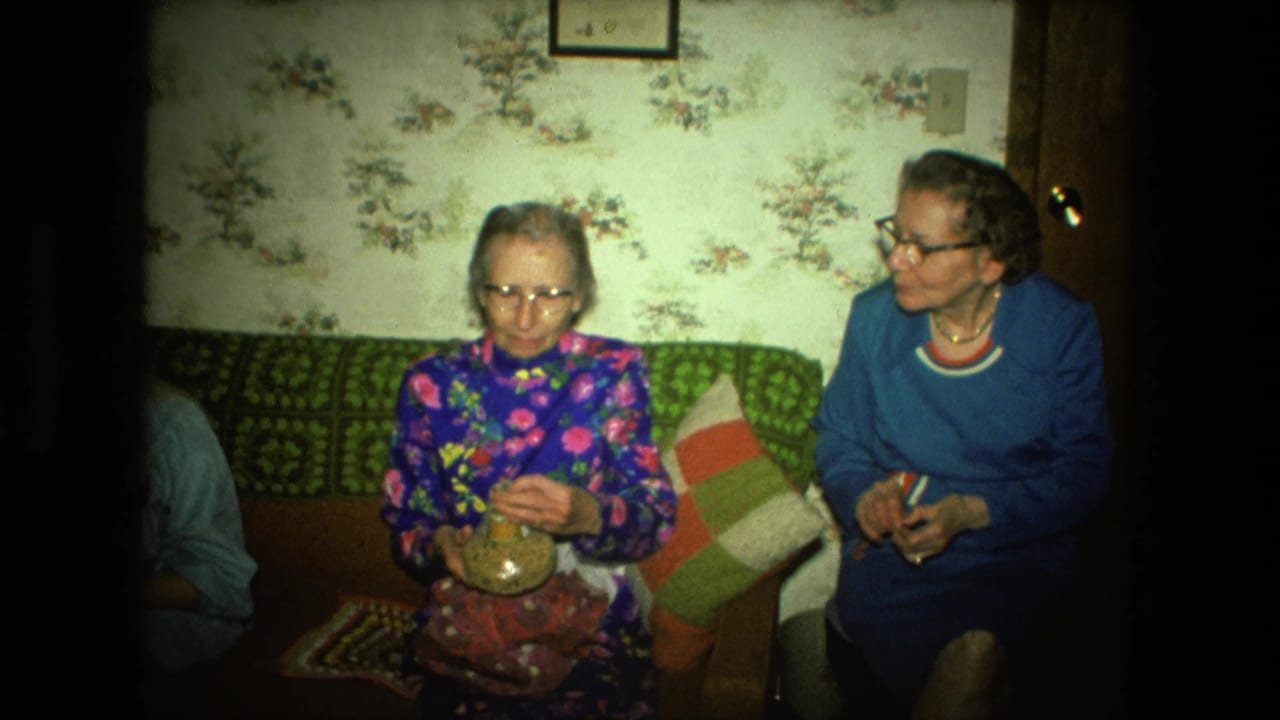 In a 1976 Fort Wayne living room, one elderly woman holds a small glass jar while another sits beside her on the couch.