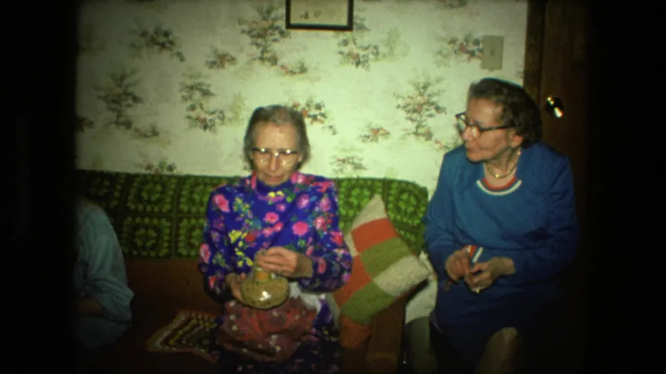 In a 1976 Fort Wayne living room, one elderly woman holds a small glass jar while another sits beside her on the couch.
