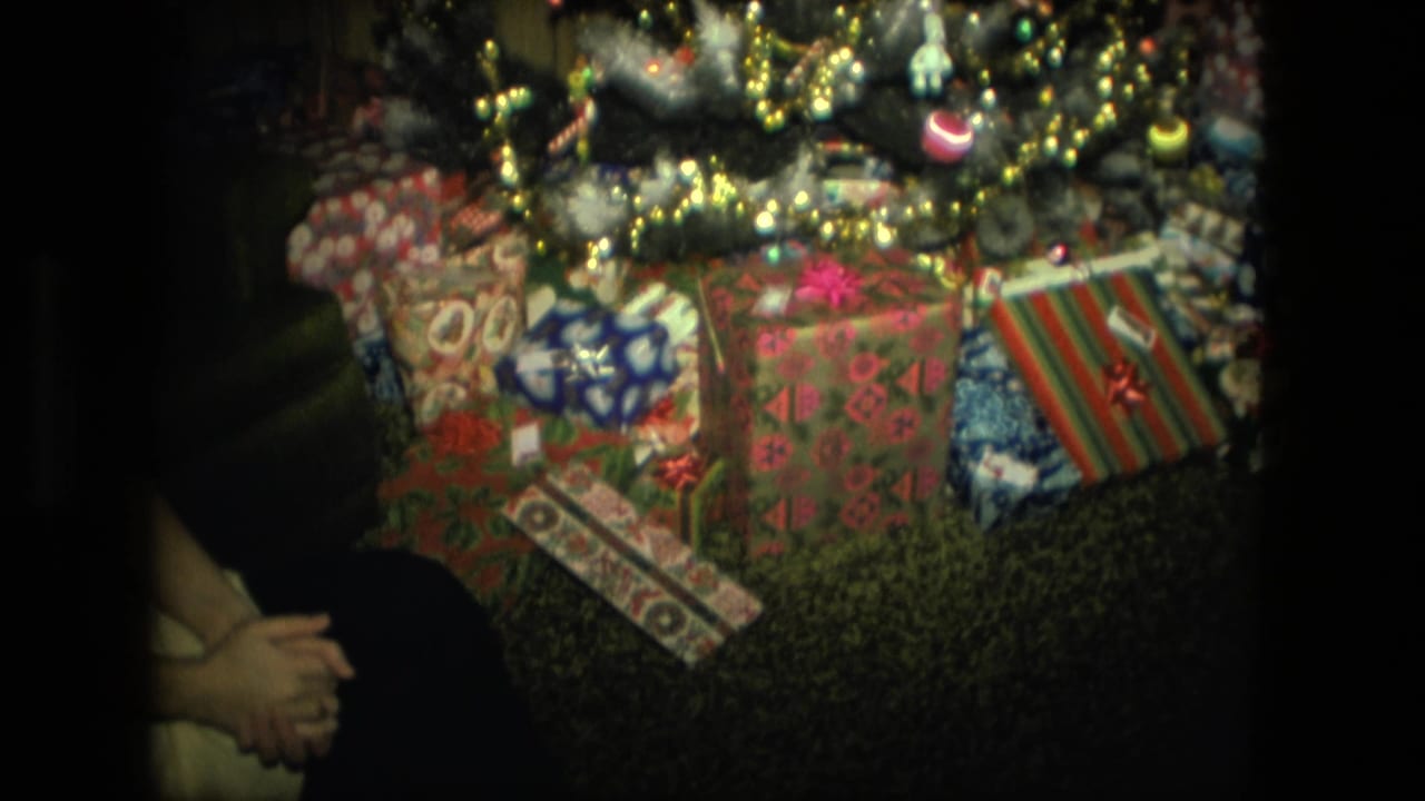 Wrapped Christmas presents under a decorated tree with part of a seated person at the left edge.