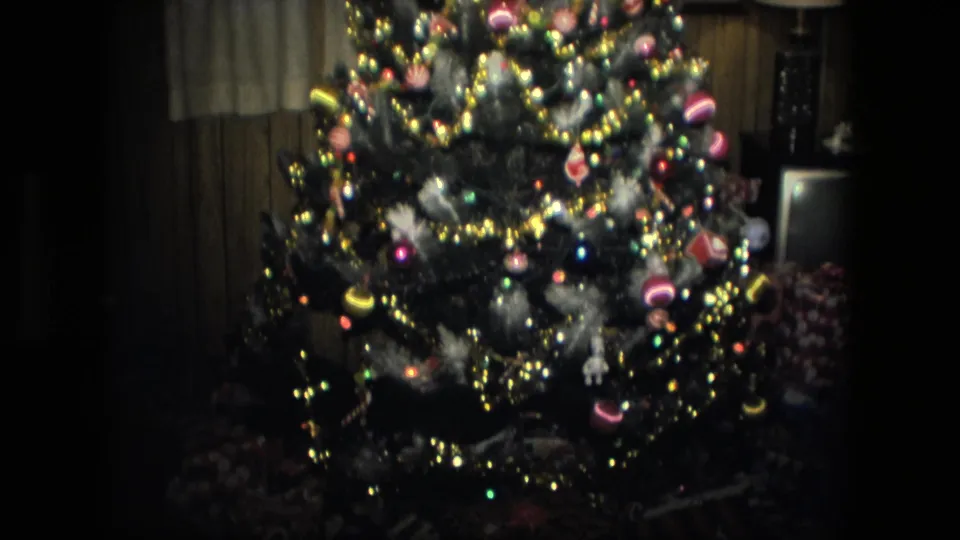 1976 Fort Wayne interior with a lit Christmas tree, shiny ornaments, tinsel, and wrapped gifts near the base.