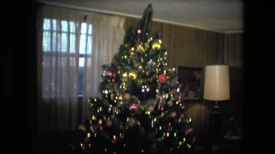 1976 Fort Wayne frame with a full decorated Christmas tree, glowing lights, ornaments, curtained window, and floor lamp.