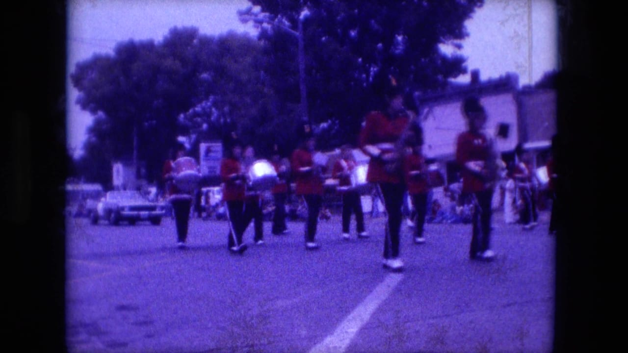 Marching band in red uniforms on a tree-lined parade street.