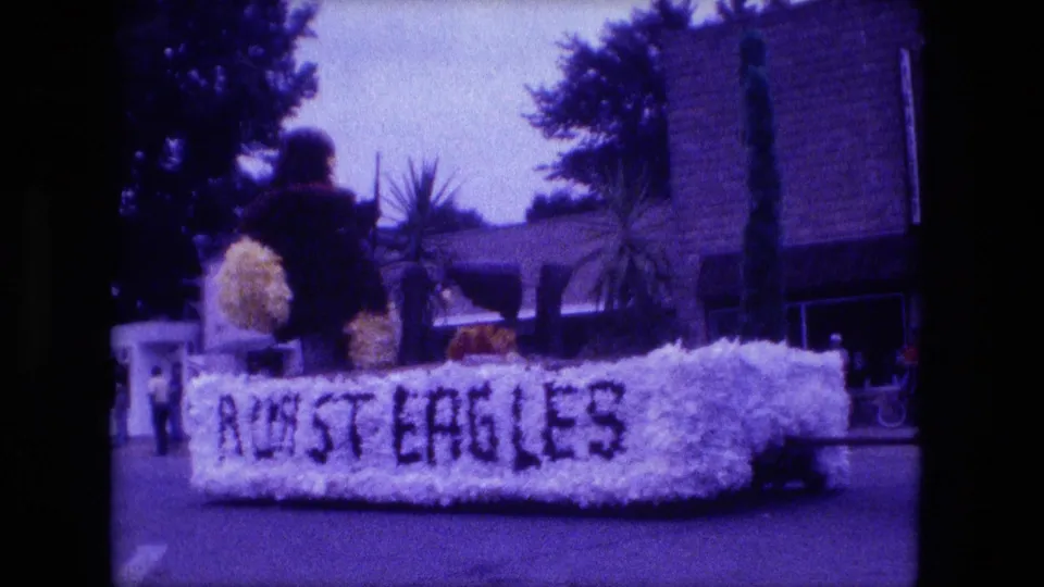The Fort Wayne parade float fills the frame, showing pale floral trim, dark lettering, and a rider or decoration above the float body.