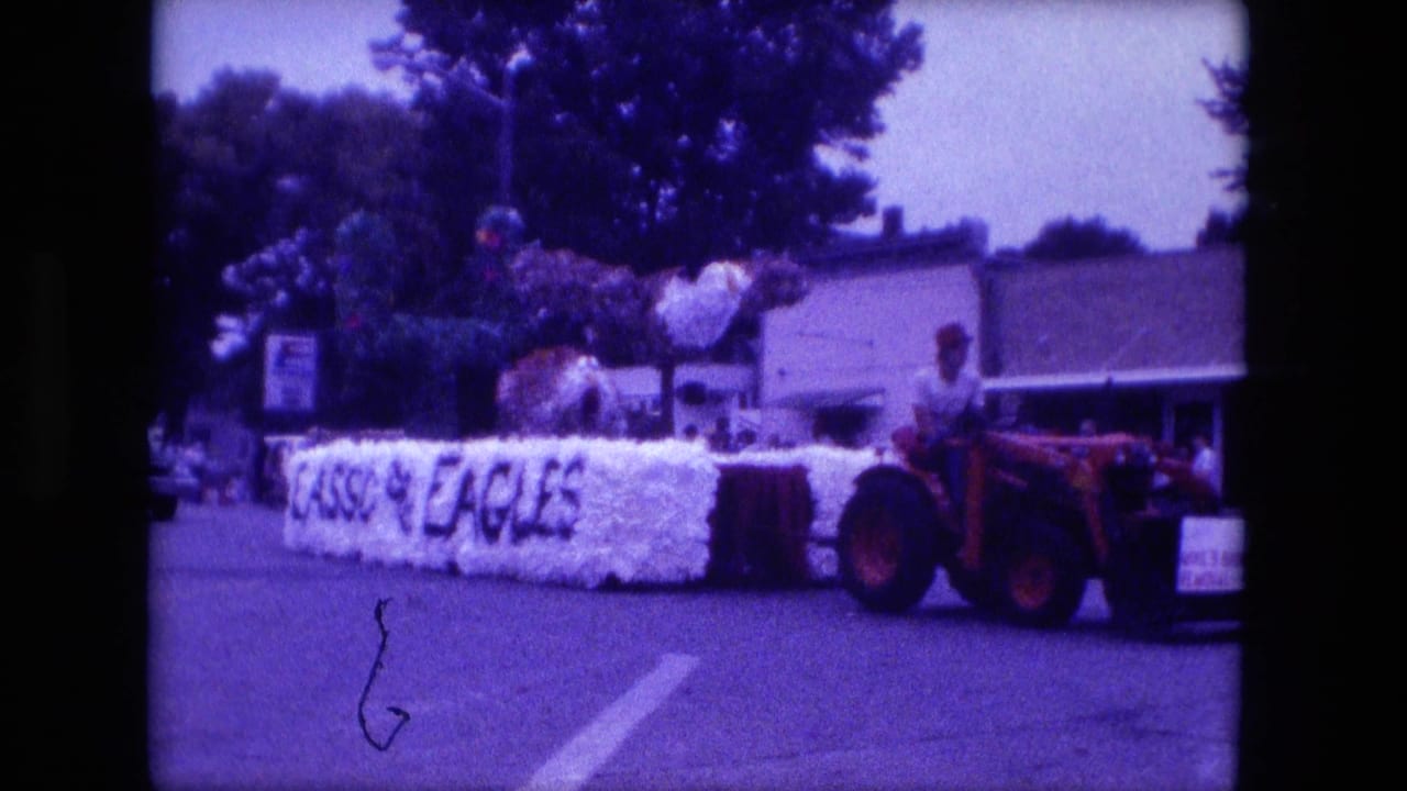 Red tractor pulling a white floral float with LASSO and EAGLES lettering on a street.