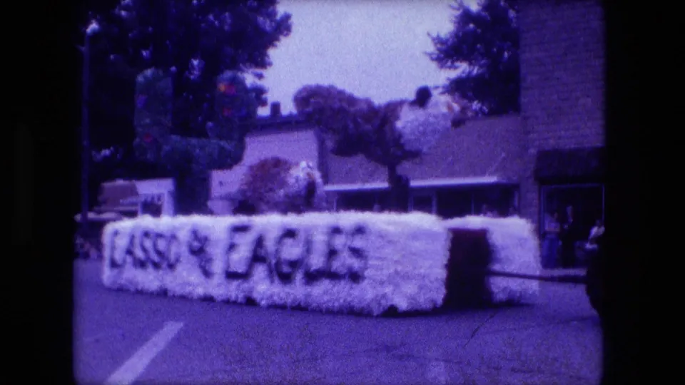 Close home-movie view of the white floral LASSO and EAGLES float passing by during the 1976 Fort Wayne parade.