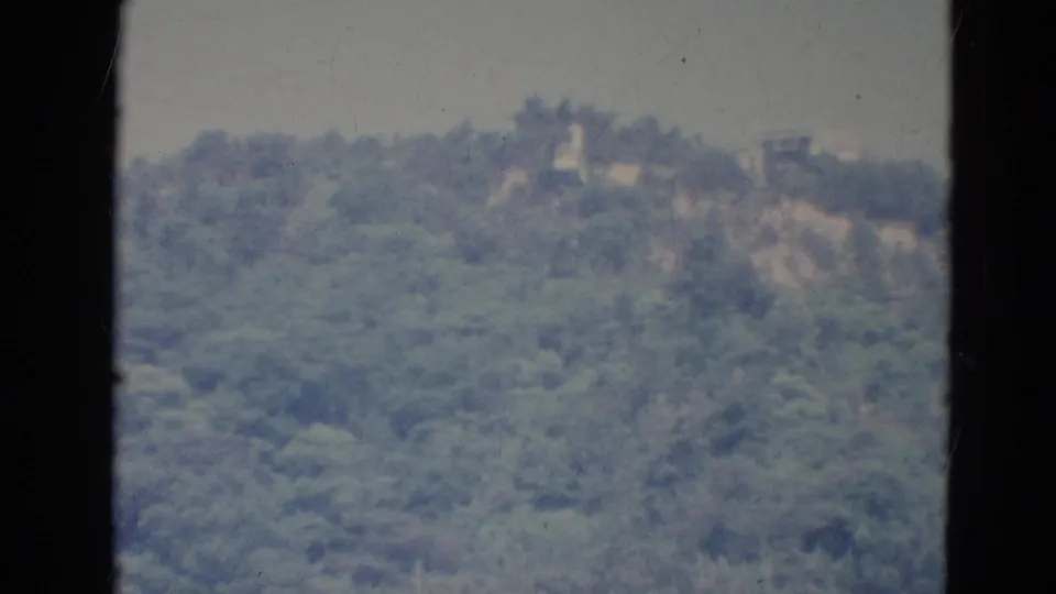 1976 Minnesota 8mm view of a wooded slope with a pale hillside break and indistinct ridge-top details.