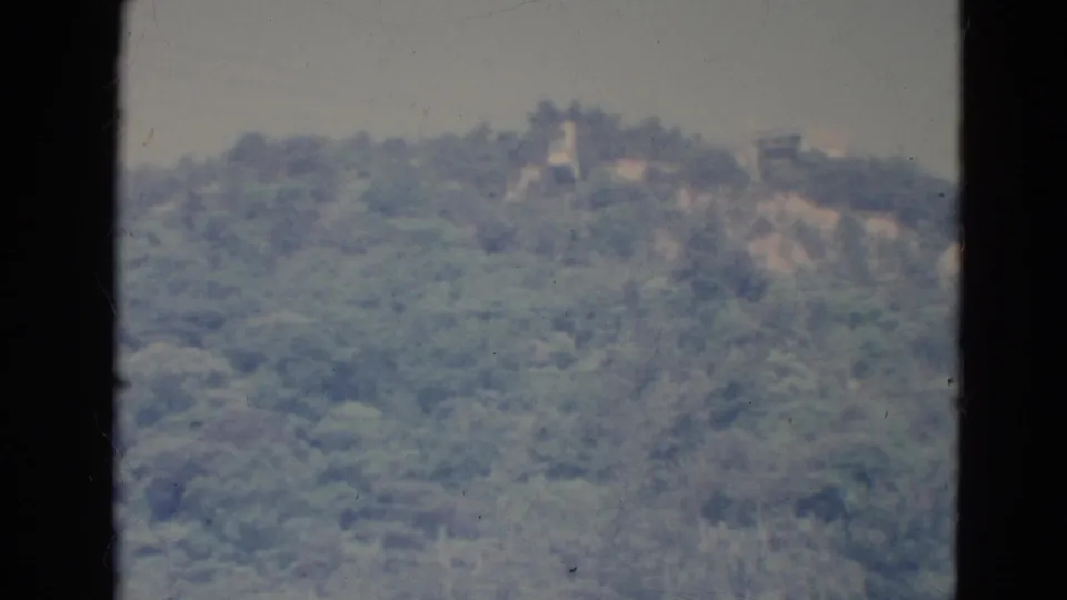 1976 Minnesota 8mm frame showing a distant wooded ridge through dark window bars, with faint structures near the horizon.