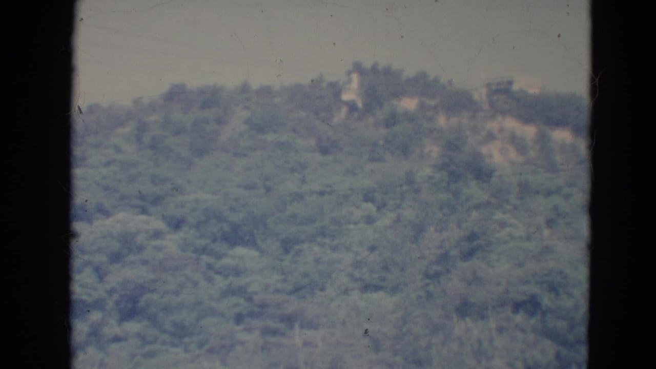 Distant tree-covered ridge with pale sky and dark vertical film border at the left.