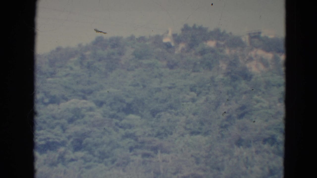 Distant forested hillside beneath a hazy sky, seen through dark 8mm film borders.