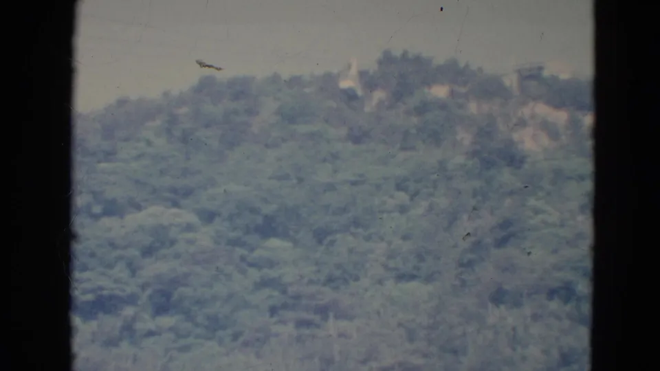 1976 Minnesota 8mm home-movie frame showing a soft, distant green ridge under a pale hazy sky with dark film borders.