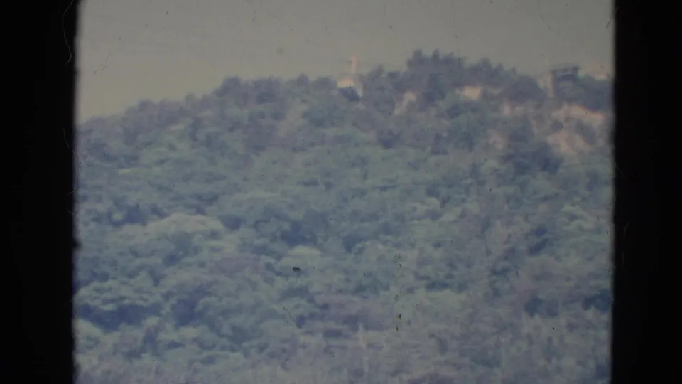 1976 Minnesota 8mm home-movie frame showing a soft wooded hillside and hazy sky with visible film grain and dust.
