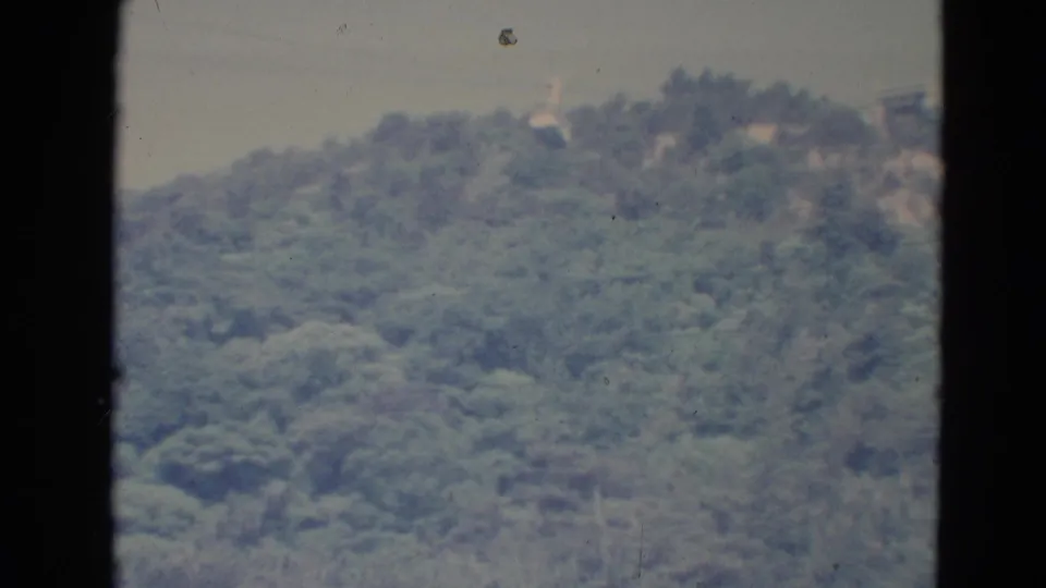 1976 Minnesota 8mm frame of a distant green hillside beneath a pale sky, with dark scan borders and visible film wear.