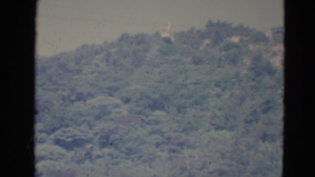 1976 Minnesota 8mm frame showing a small cable car suspended above a soft, forested hillside under hazy sky.