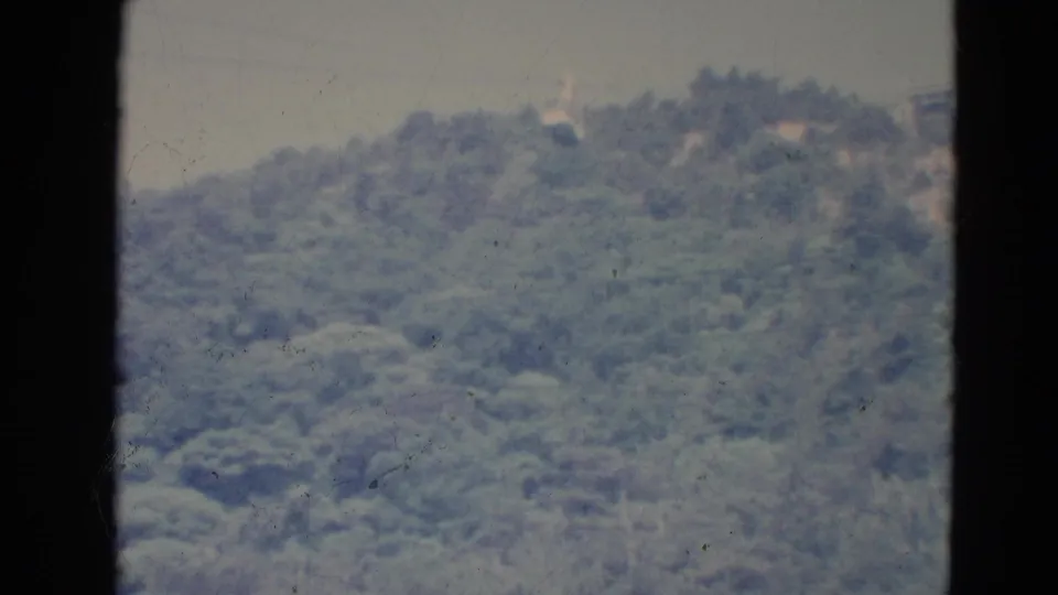 1976 Minnesota 8mm frame showing a small cable car suspended above a soft, forested hillside under hazy sky.