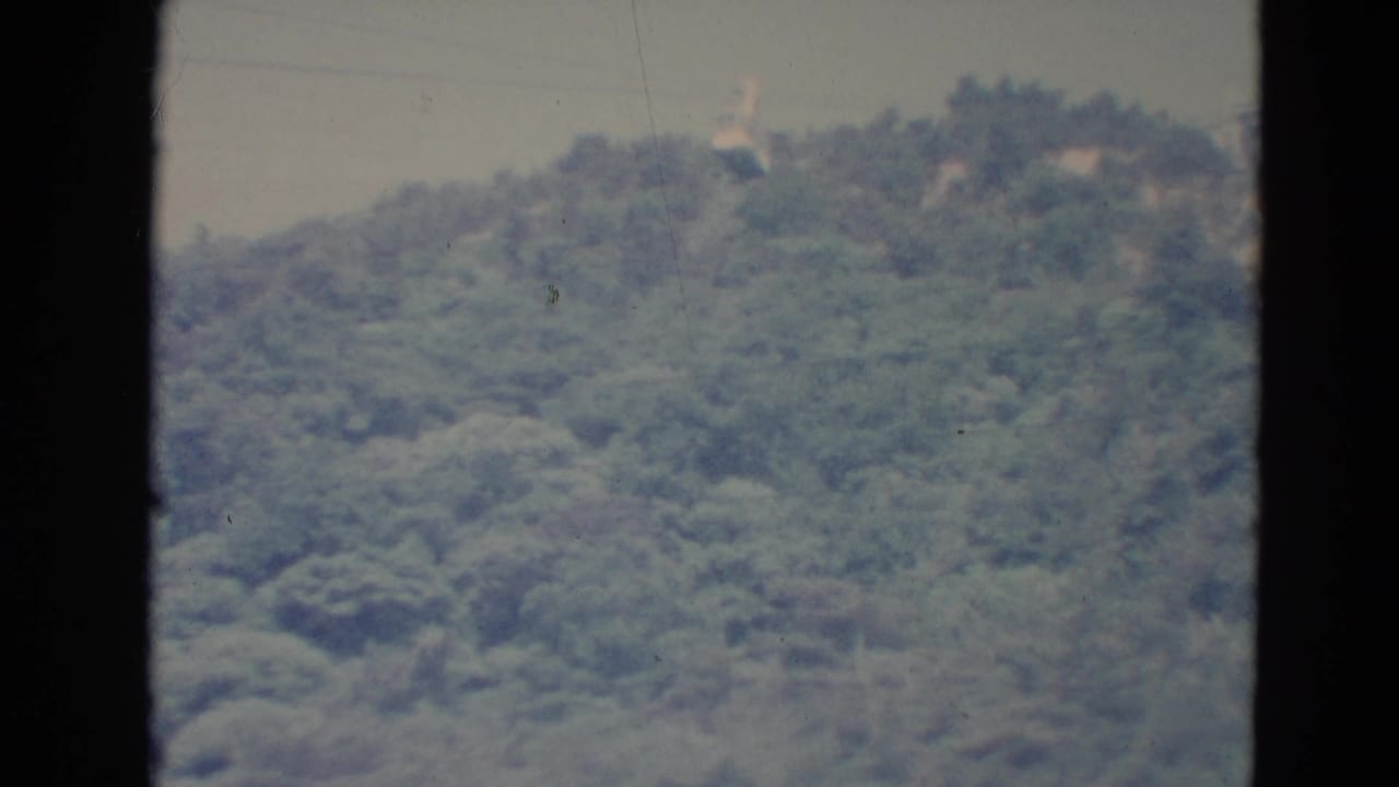 A small cable car appears near the upper ridge line of a wooded Minnesota hillside in a soft 1970s home-movie frame.