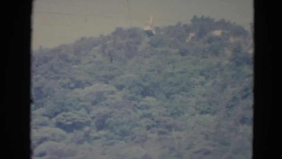 A small cable car appears near the upper ridge line of a wooded Minnesota hillside in a soft 1970s home-movie frame.