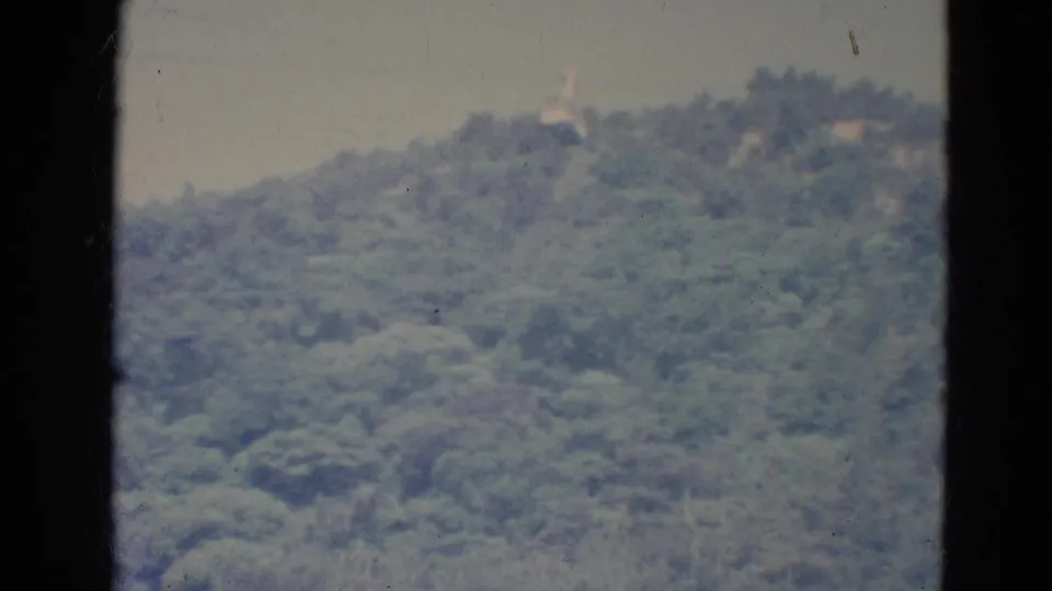 1976 home-movie frame from Minnesota with a distant cable car moving over a dense, green hillside.