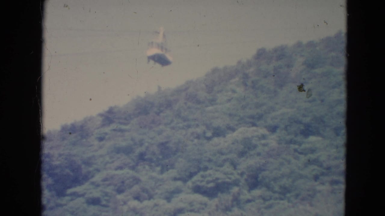 Distant gondola above a wooded hillside, framed by dark vertical edges.