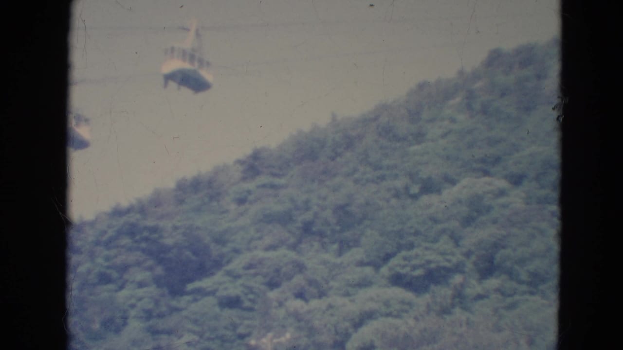 Two cable cars suspended above a forested hillside, framed by dark film edges.