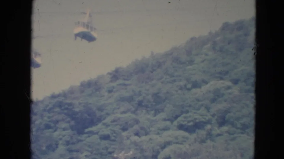 1976 Minnesota 8mm frame showing distant cable cars over a wooded slope with soft focus and faded color.