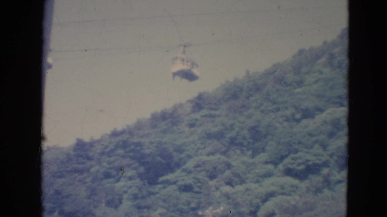 1976 Minnesota 8mm frame showing a small skyride cabin crossing above a tree-covered slope through a dark window or gate edge.