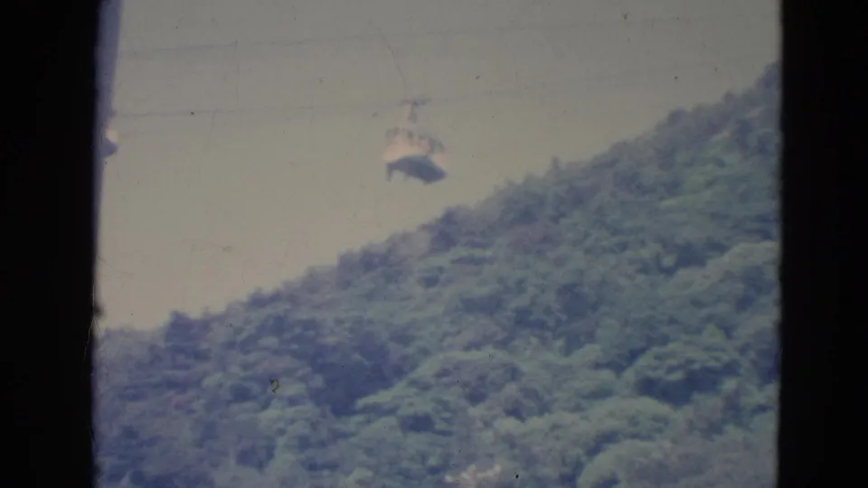 1976 Minnesota 8mm frame showing a small skyride cabin crossing above a tree-covered slope through a dark window or gate edge.
