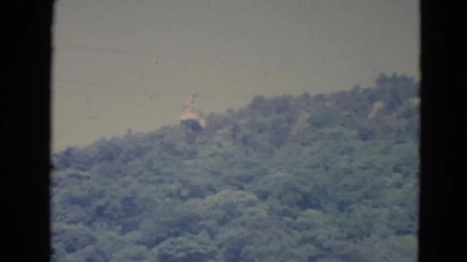 Soft 8mm frame from Minnesota in 1976 showing a cable car over a green hillside, viewed through a narrow framed opening.