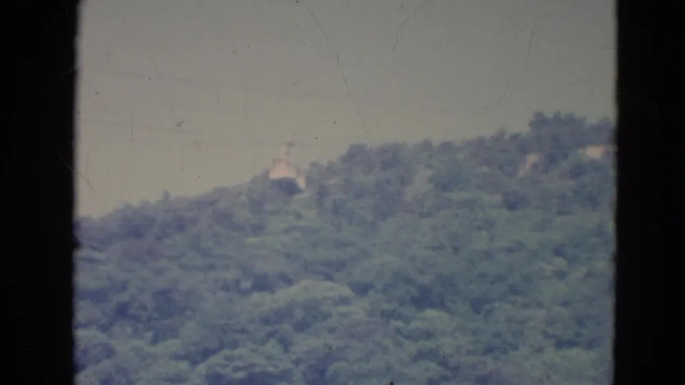 1976 Minnesota 8mm frame showing a small skyride cabin crossing above dense trees, with soft exposure and dark frame borders.